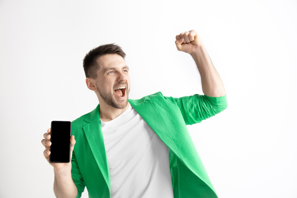 Código promocional 1xBet (bônus de boas-vindas de até $130) 2 its cool good news that like me young handsome man showing smartphone screen signing ok sign isolated gray background human emotions facial expression advertising concept 1