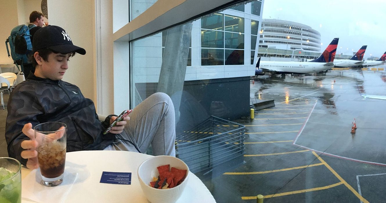 Viajante sentado à mesa em um saguão de aeroporto com vista para a pista