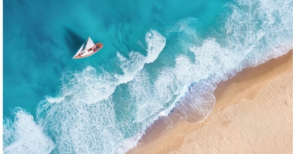 an aerial view of a sailboat off a caribbean beach